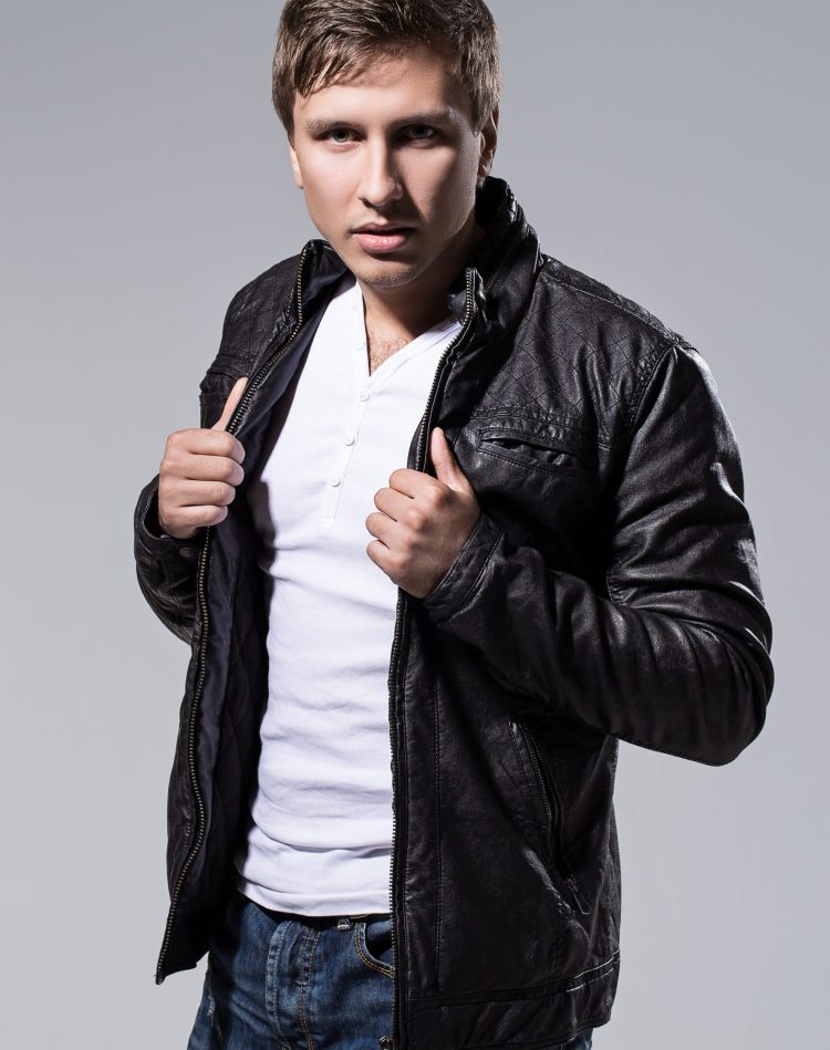 Handsome man in leather jacket, jeans and white t-shirt is posing over a grey background